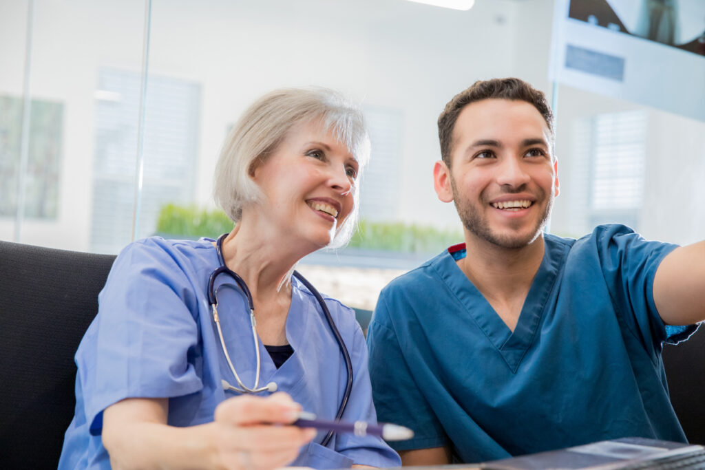 Senior adult Caucasian female doctor with gray hair is smiling while examining a patient x-ray during a consultation with a young adult Hispanic male doctor.