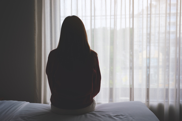 Rear view image of a woman sitting alone on a bed in bedroom stock photo