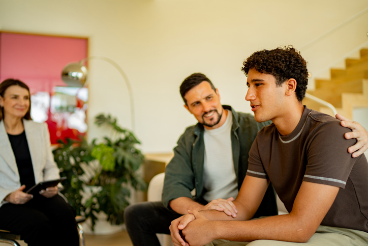 Teenage boy being comforted by father during psychotherapy session